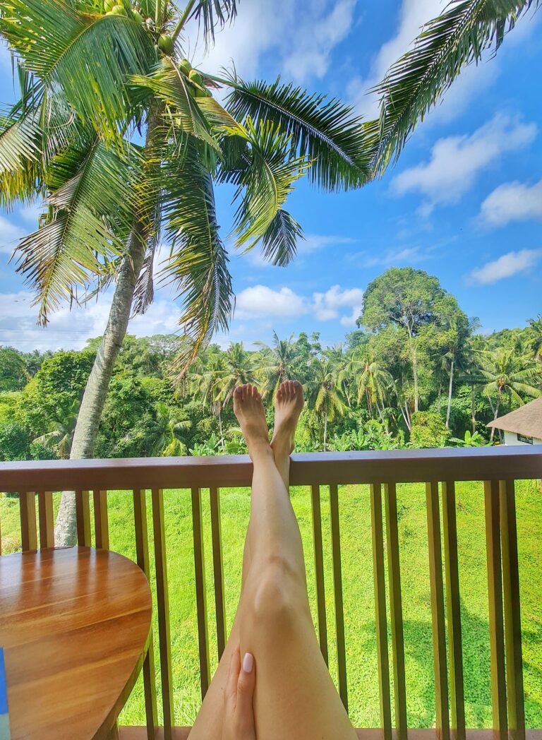 Person relaxing on a balcony in Ubud with legs streched out, overlooking lush palm trees and tropical greenery