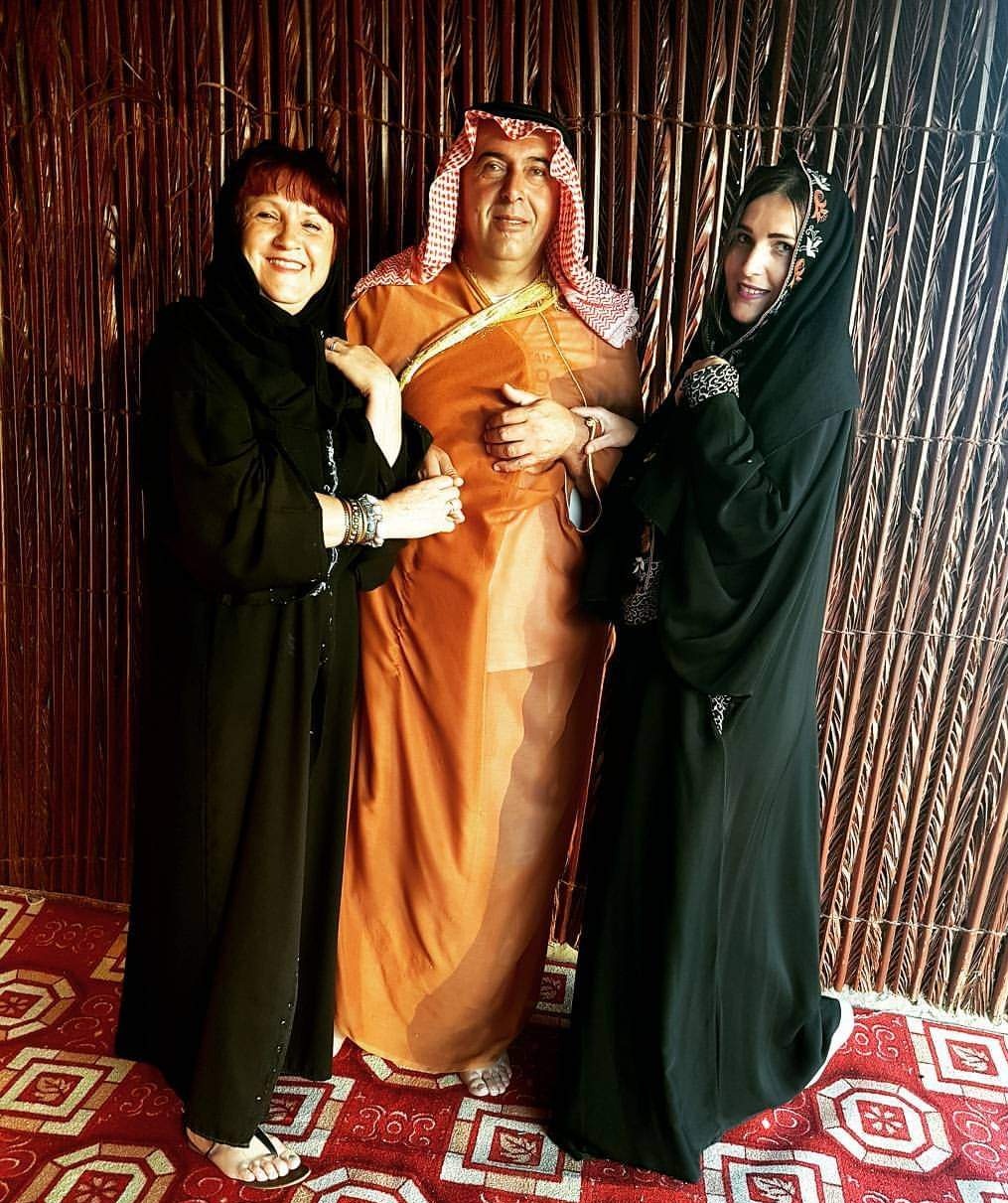 A family of three wearing traditional-style costumes posing together during a desert safari photoshoot in the desert landscape.