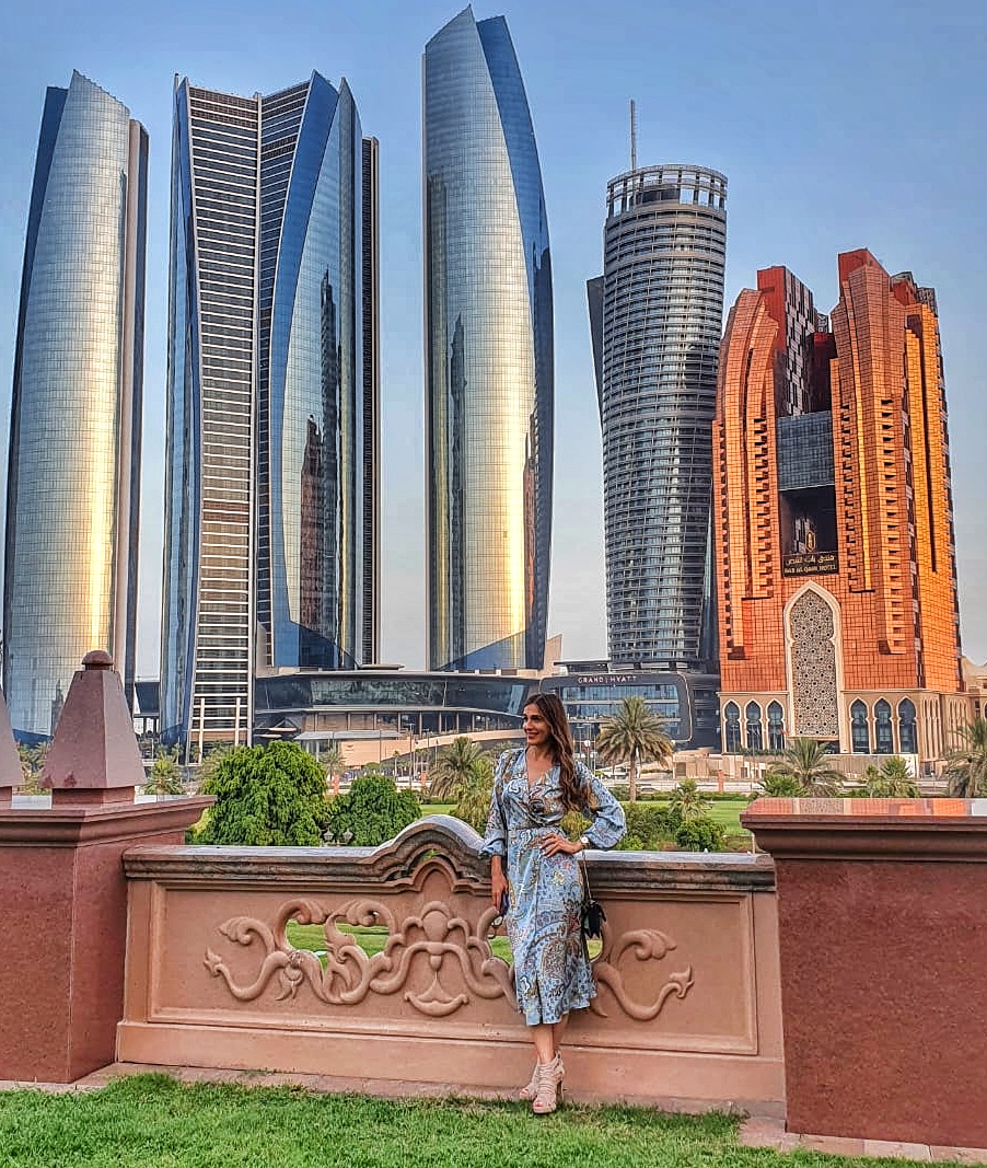 Person standing in front of Etihad Towers and Bab Al Qasr Hotel in Abu Dhabi with a modern city skyline in the background.
