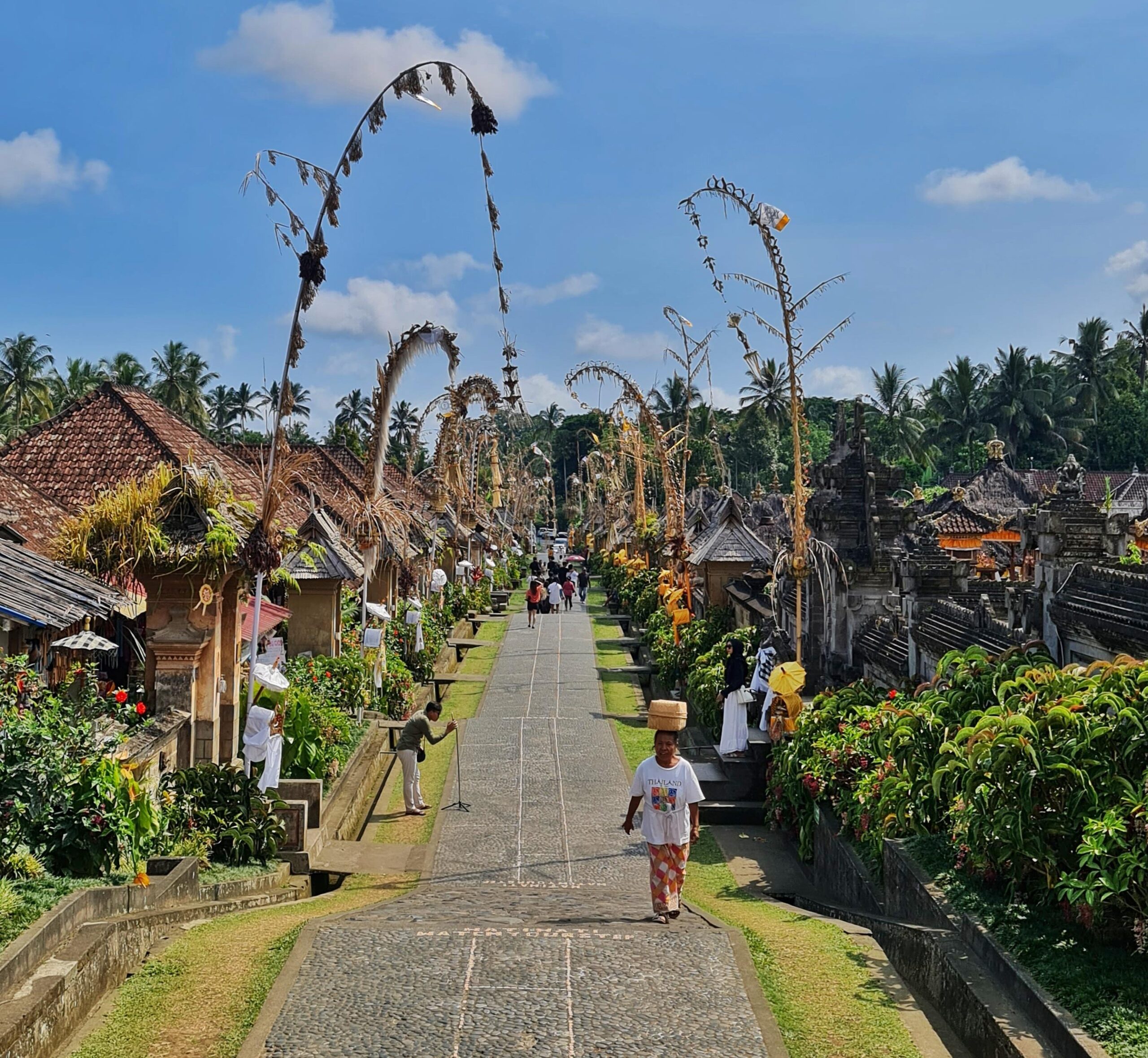Traditional street with a Balinese woman carrying offerings on her head, lined with bamboo houses