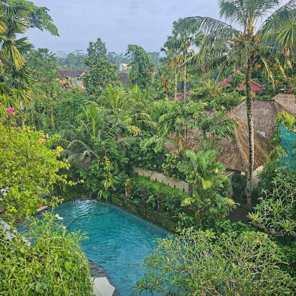 Resort pool in Bali with lounge chairs and villas in the background surrounded by tropical greenery