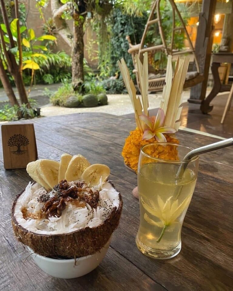 View of a lush, greenery-filled Ubud Bali restaurant with a smoothie bowl and drink