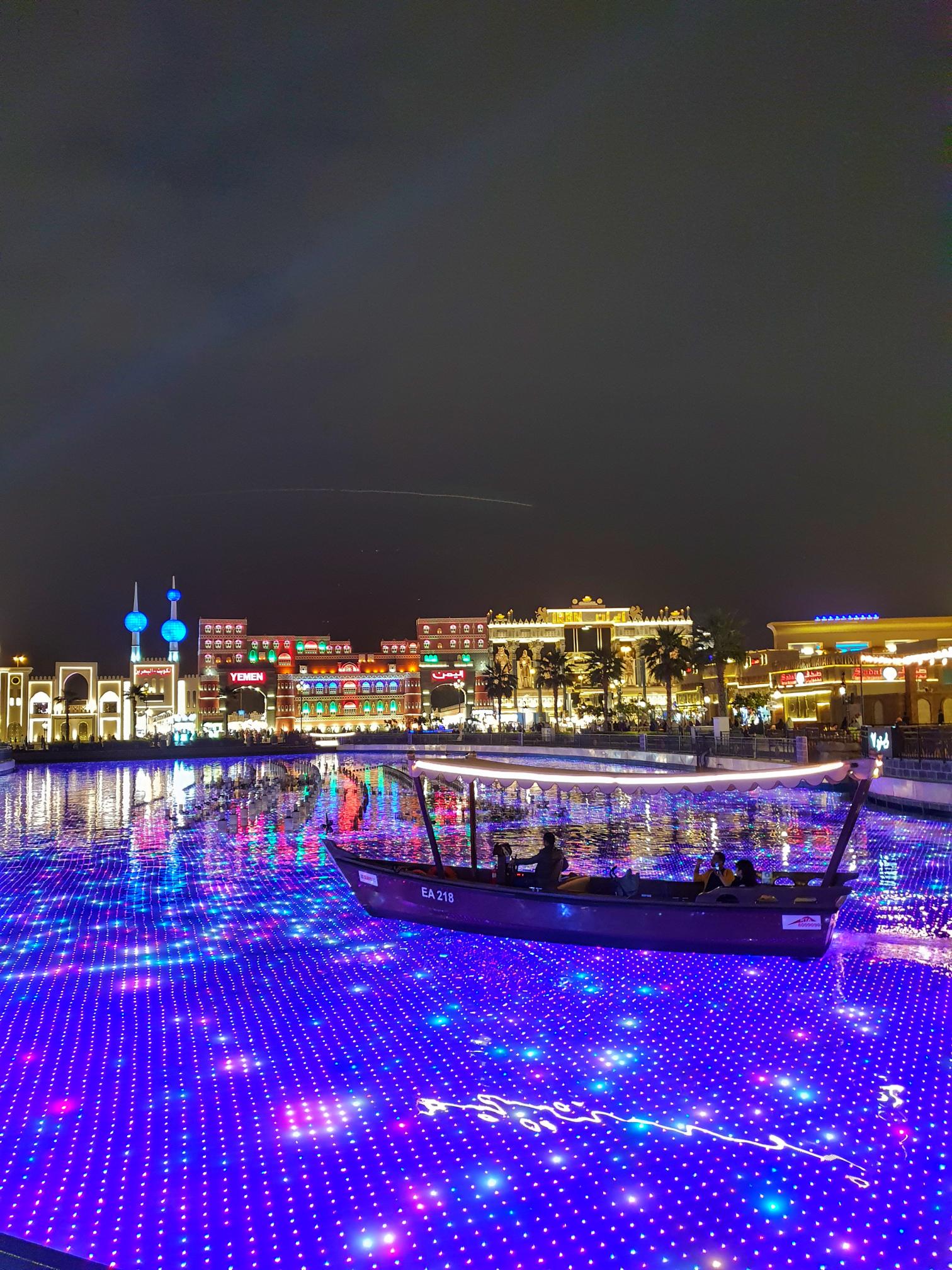 Night view of Global Village with lights, water canal, and traditional boat ride
