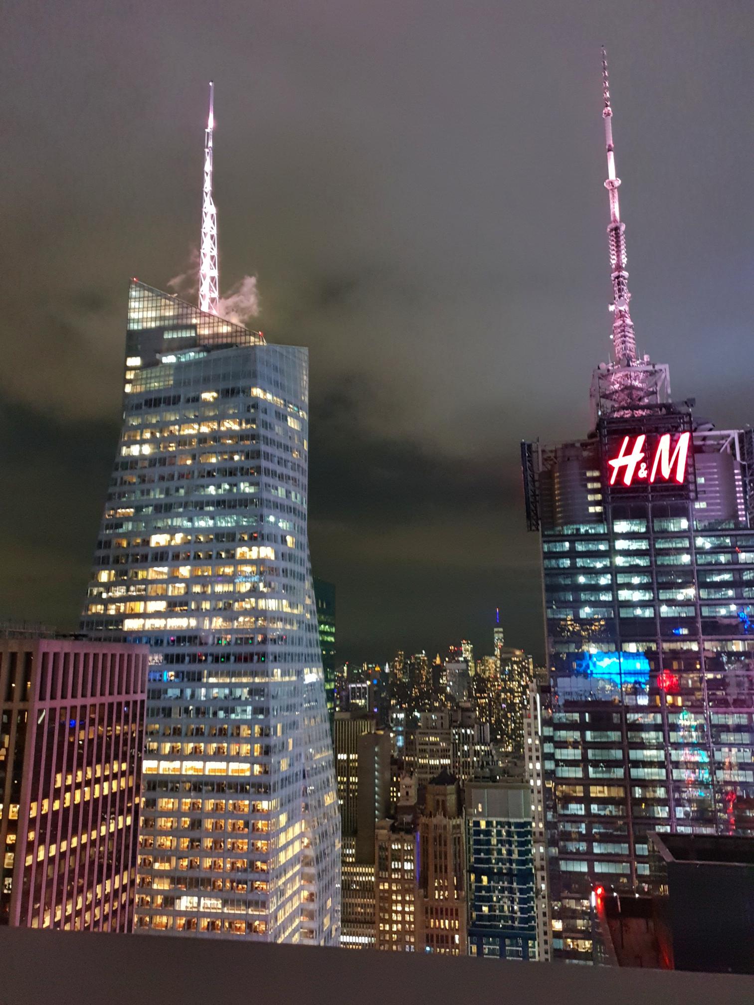 Night view from a Midtown rooftop bar with the H&M building in the background.