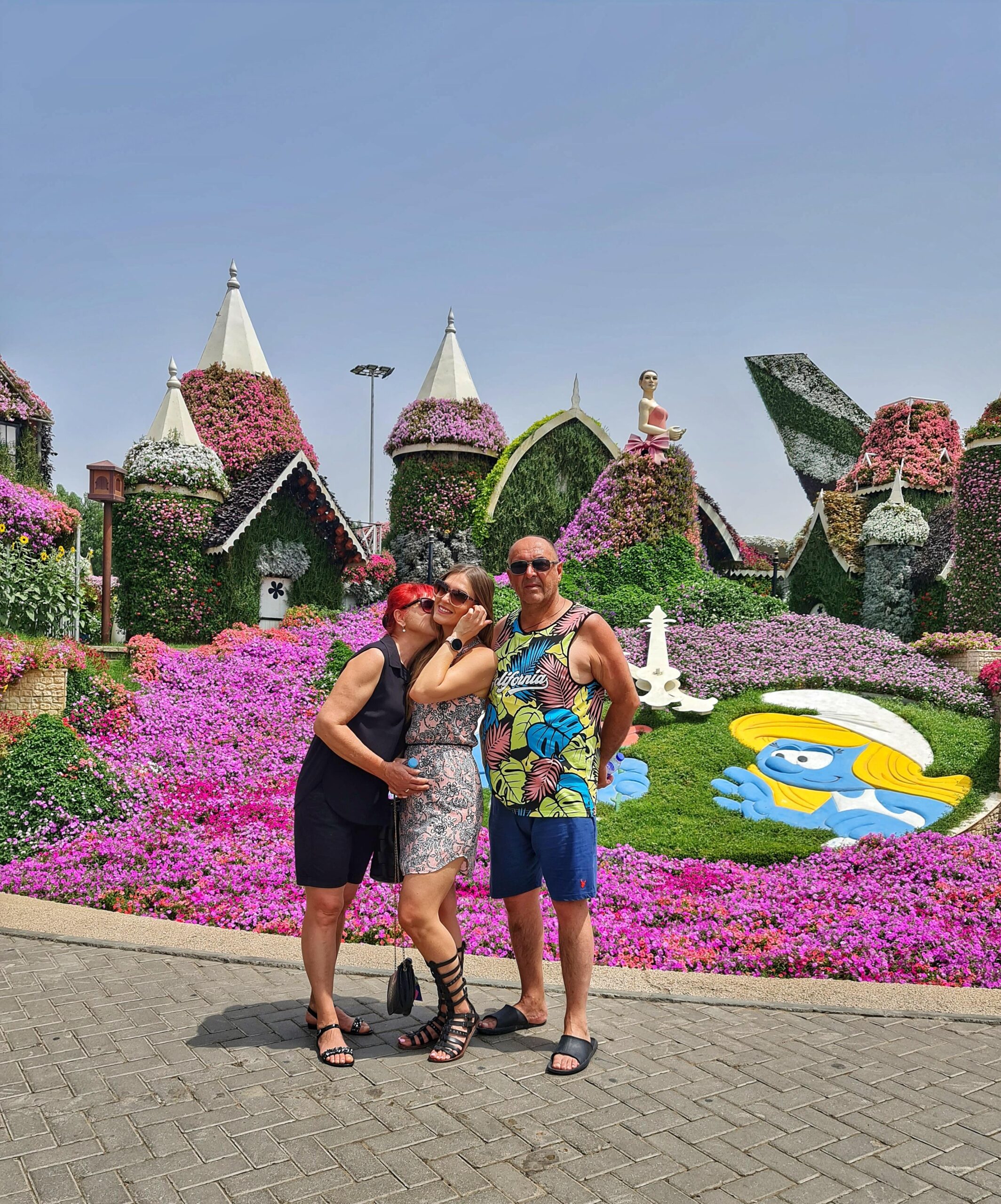 Woman with parents at Dubai Miracle Garden with colorful floral displays in the background