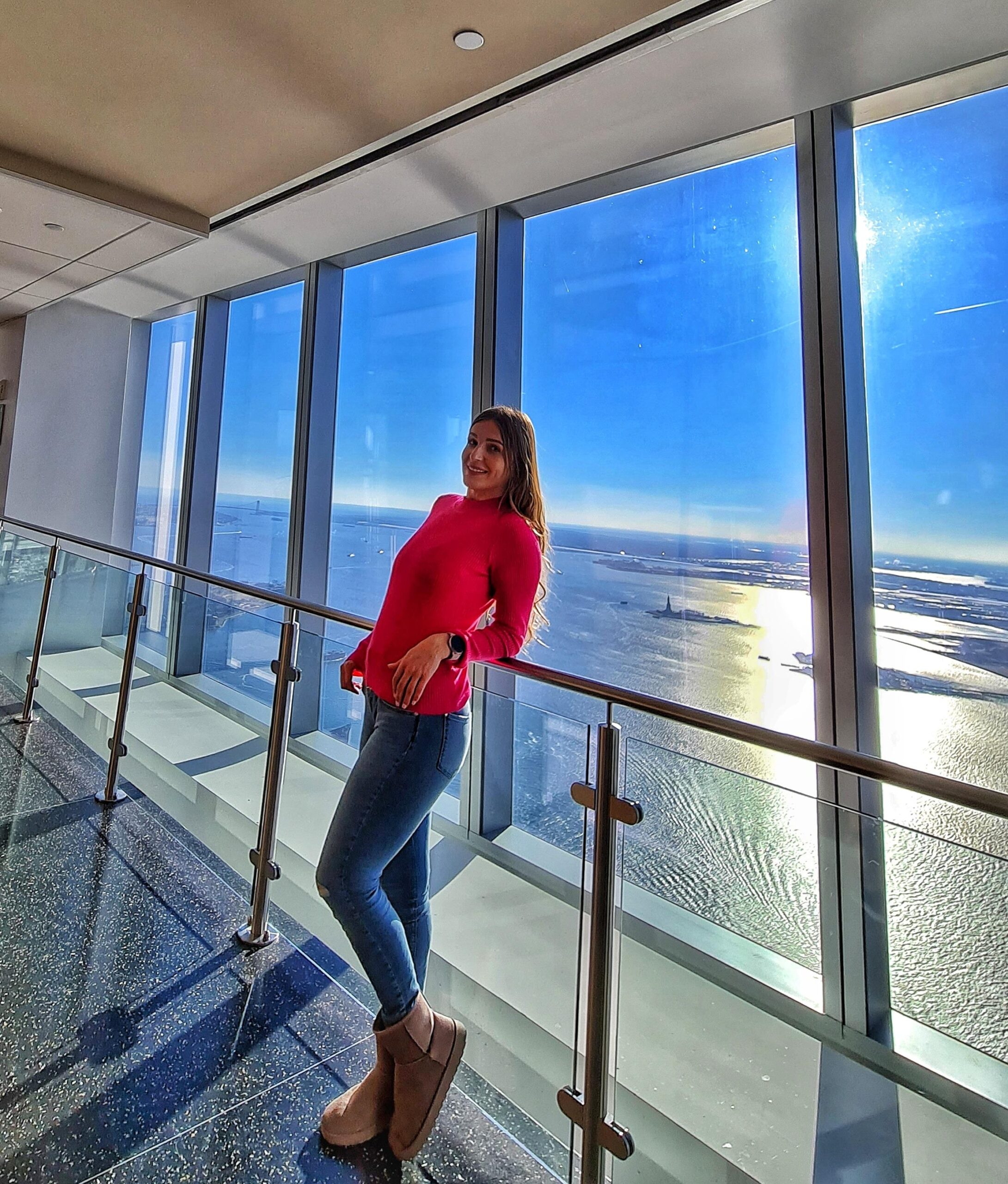 Standing at One World Observatory in New York City with panoramic skyline views.