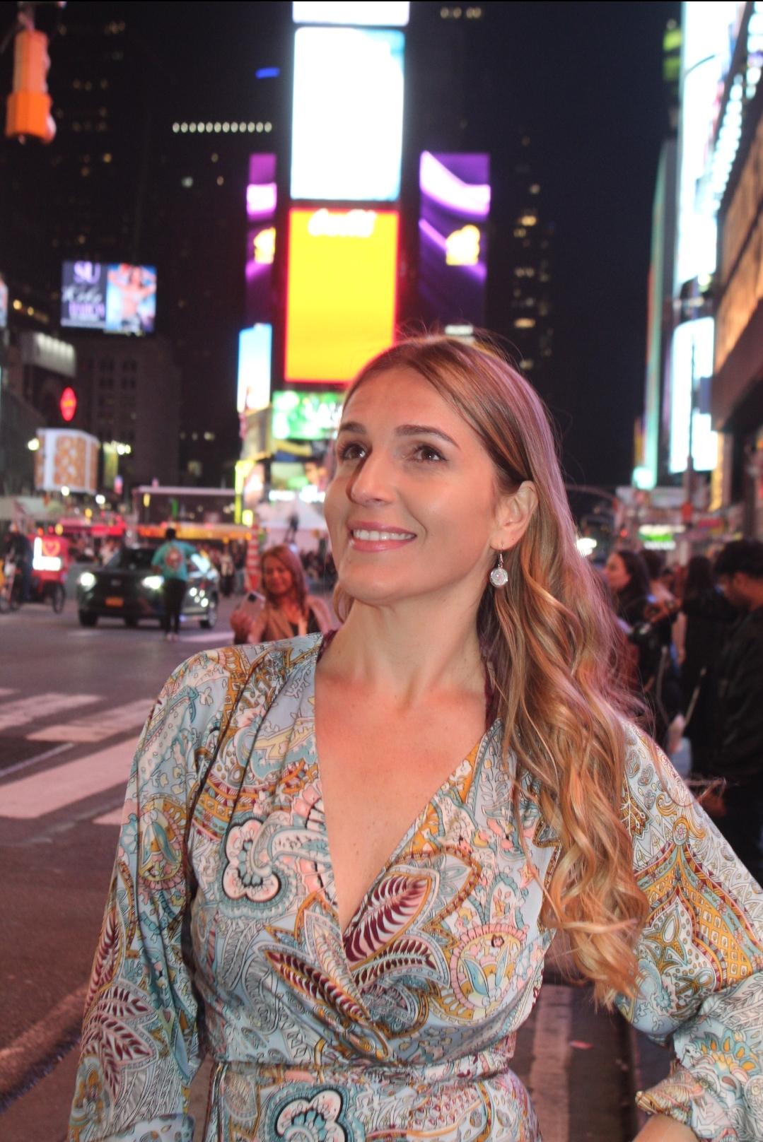 Portrait of me in Times Square being photographed, with Manhattan skyscrapers and city lights behind me.
