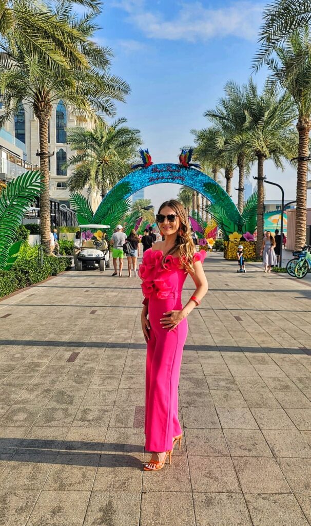 Woman in pink jumpsuit in Palm Jumeirah, Dubai with palm trees in the background.